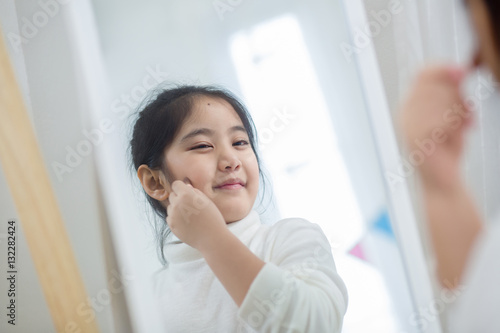 Pretty Asian child doing make up front of the mirror