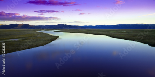 Fototapeta Naklejka Na Ścianę i Meble -  Wetlands in California at Sunset. River leads off into the distance towards mountain range with colorful reflections in water.