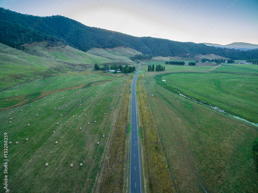 Aerial view of Omeo highway among green fields and hay bales in Mitta Mitta Valley, Victoria, Australia