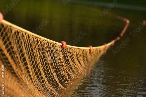 Large sunlit fishing net with red floats cast diagonally across dark green water 