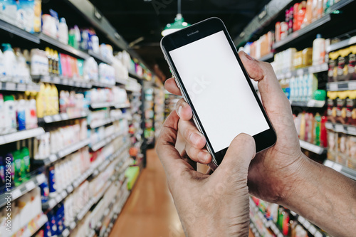 Man hands holding smart phone with blank screen in supermarket, light bokeh background.