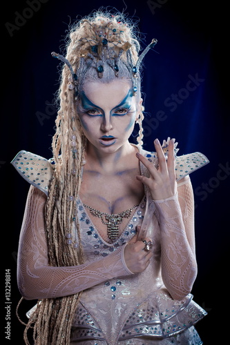 emotional actress woman in makeup and costume queen of elves or snow queen on blue-black background photo