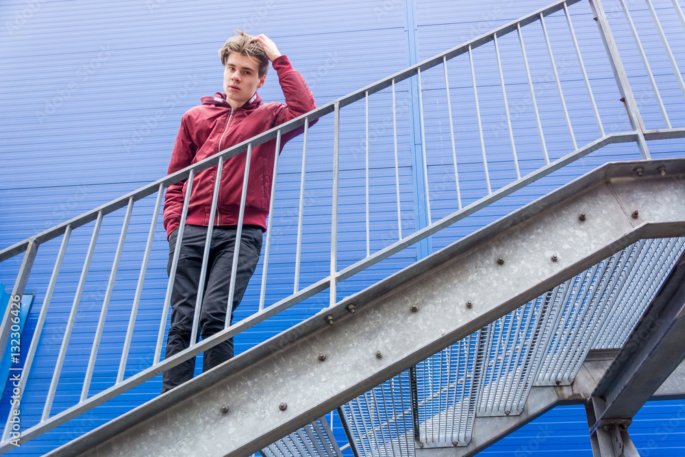 Bored teenager boy standing on stairs over blue building