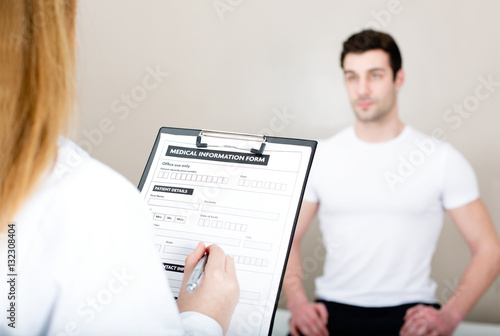 Female doctor visiting her male patient and compiling medical information form in medical center.