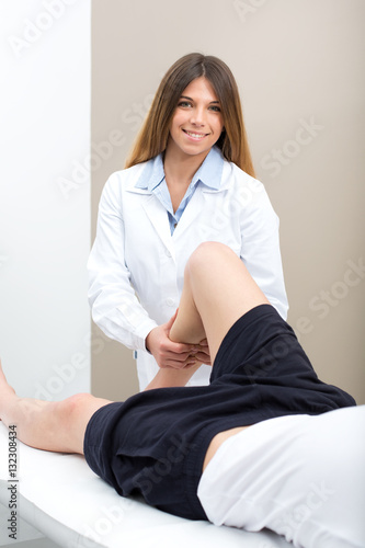 Female doctor physiotherapist smiling and practicing massage to her leg male patient in medical center.