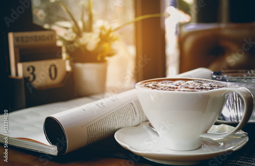 Cup of hot cappuccino with newspaper and calendar on the table,