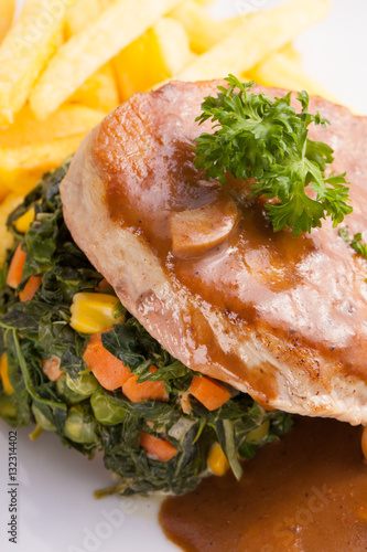 a dish of pork sirlion steak served with brown sauce and sauté spinach and french fries in a nice dish. photo