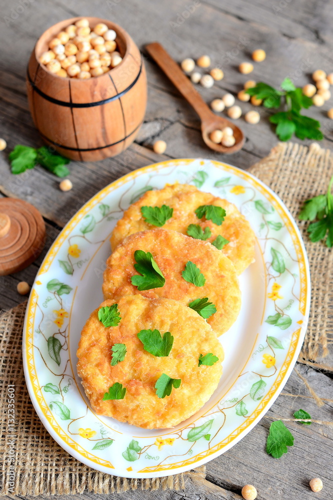 Fried pea patties on a plate. Spicy vegan patties cooked from yellow dried peas and decorated with green parsley. Small decorative barrel and spoon on old wooden background. Vegan dish recipe. Closeup Fried pea patties on a plate. Spicy vegan patties cooked from yellow dried peas and decorated with green parsley. Small decorative barrel and spoon on old wooden background. Vegan dish recipe. Closeup