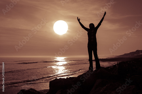 Silhoetted woman at sunset with her arms raised photo
