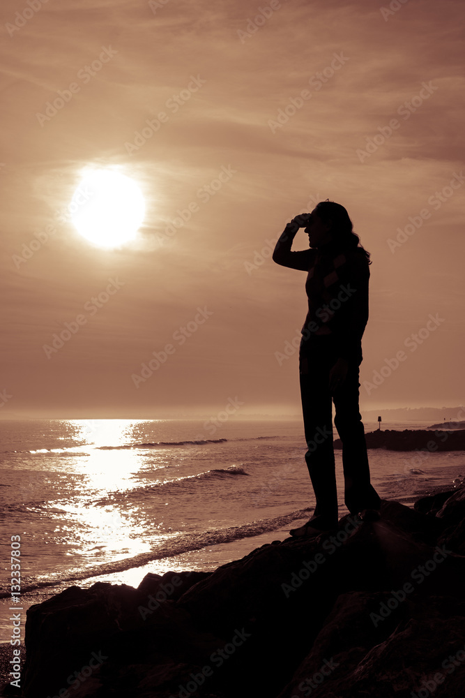 Fototapeta premium Silhouetted female figure shields her eyes as she looks at the s