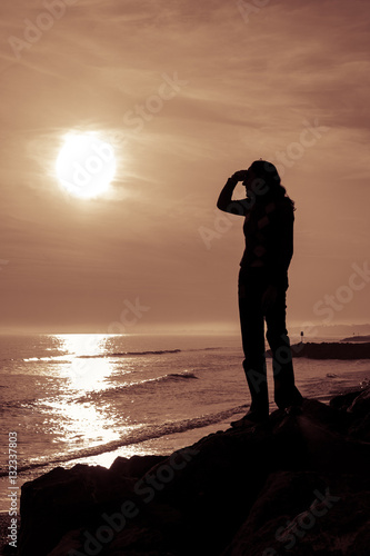 Silhouetted female figure shields her eyes as she looks at the s