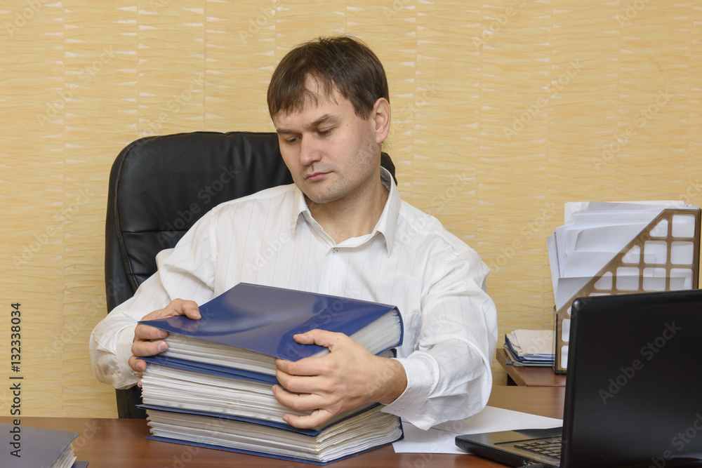 The man at the desk in the office pulls to carry documents in folders The man at the desk in the office pulls to carry documents in folders