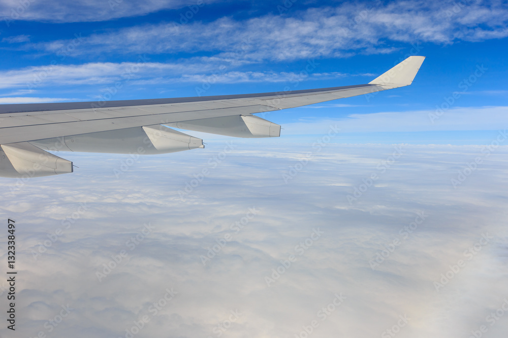 Fototapeta premium A view of wing of airplane from window above clouds and blue sky
