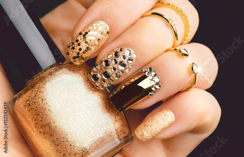 Golden nail art manicure. Holiday style bright manicure with gems and sparkles. Bottle of nail Polish. Fashion rings photo