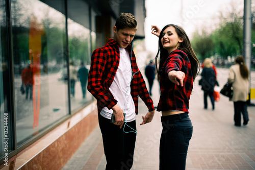 Two happy trendy teenage friends walking and dancing in the city  listening to the music with headphones  talking each other and smiling. Lifestyle  friendship and urban life concepts.