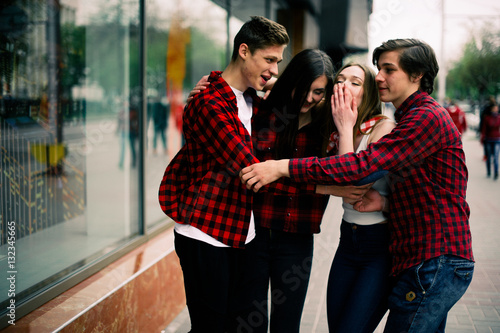 Four happy trendy teenage friends walking in the city, talking each other and smiling. Lifestyle, friendship and urban life concepts. © dashamuller