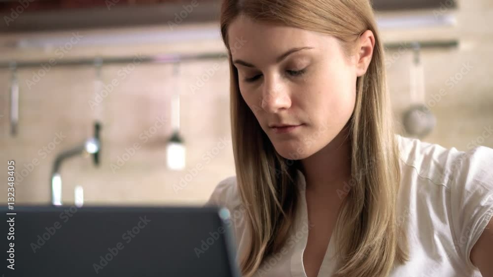 Beautiful young woman with laptop. Typing, browsing Internet and smiling. Morning Kitchen Breakfast.