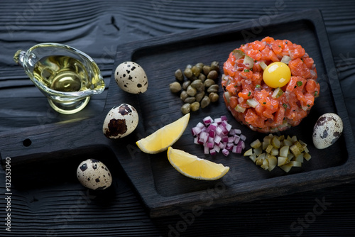 Salmon tartar on a black wooden serving board, studio shot