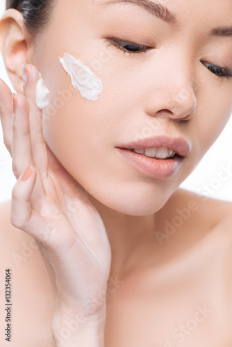 Beautiful positive woman applying cream on her face