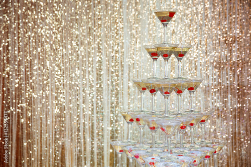 Sparkling champagne pyramid, tower of glasses at the party in front of golden wall 