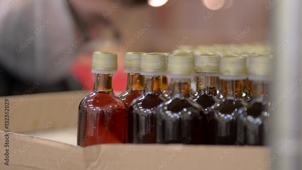 A factory worker packs a box of filled maple syrup bottles ready to ship. A factory worker packs a box of filled maple syrup bottles ready to ship.