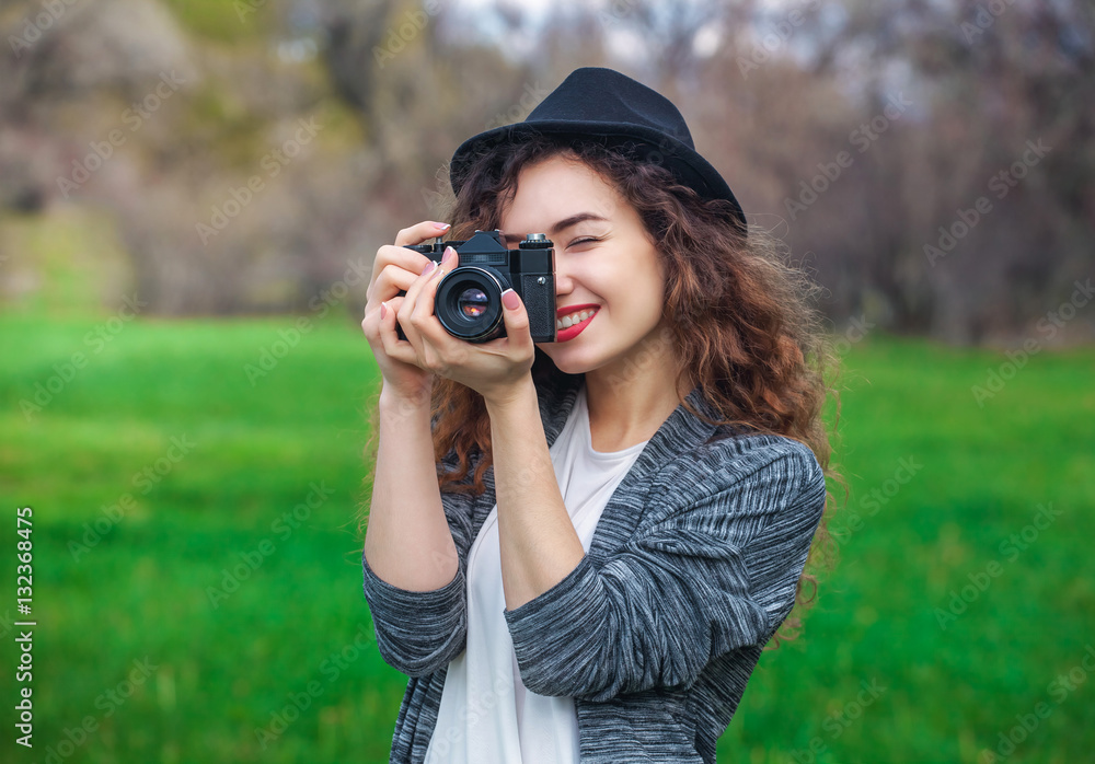 Beautiful girl-photographer with curly hair holding an old camera and take a picture, in the spring outdoors in the park. The concept of tourism and travel.
