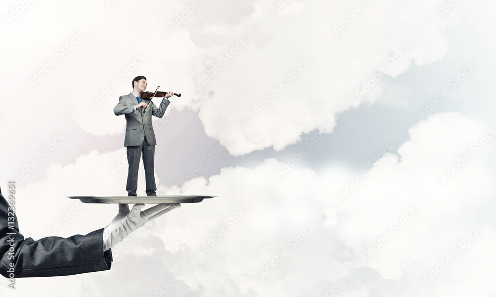 Businessman on metal tray playing violin against blue sky background Businessman on metal tray playing violin against blue sky background