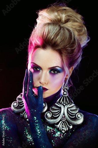 Young attractive blonde girl in bright art-makeup  in purple tones. Rhinestones and glitter body painting.