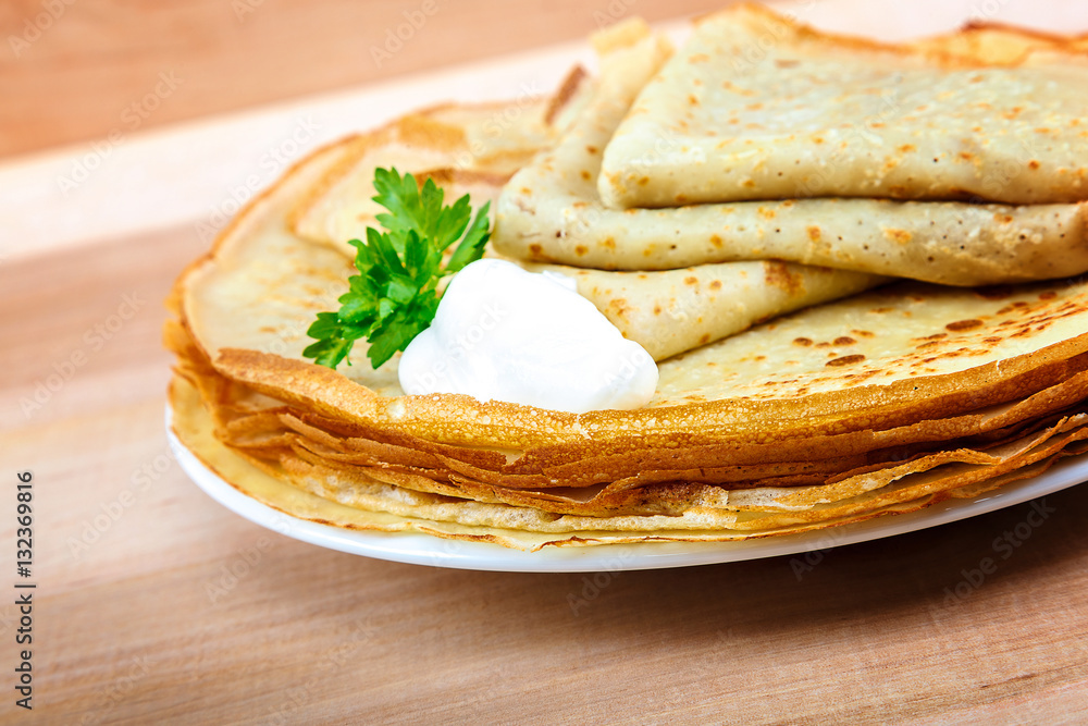 Pancakes with sour cream in a bowl on a wooden