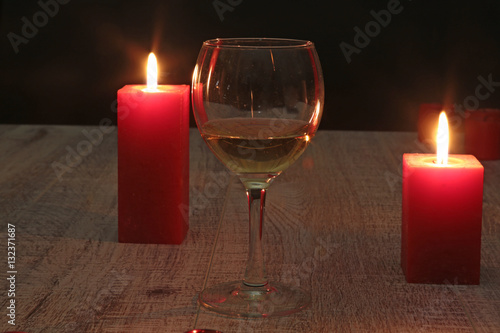 glass of wine or cognac and red candle on a wooden background.
