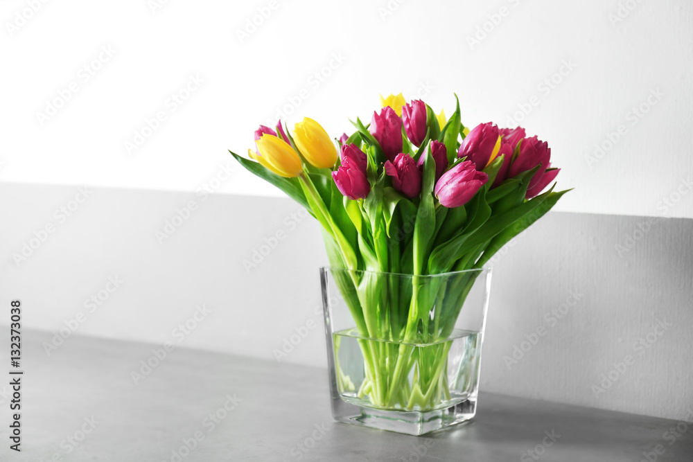 Glass vase with bouquet of beautiful tulips on color background Glass vase with bouquet of beautiful tulips on color background