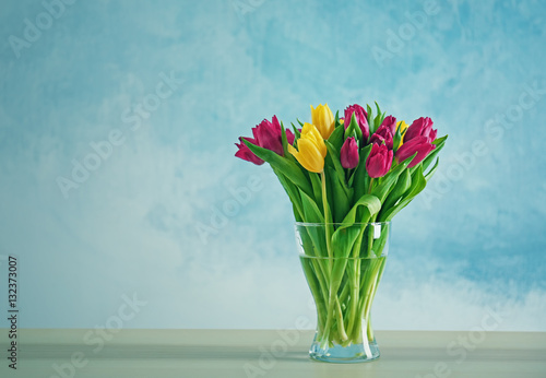 Glass vase with bouquet of beautiful tulips on color background