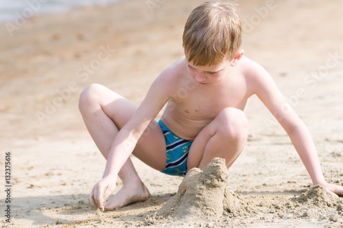 Little boy on the beach plays with sand