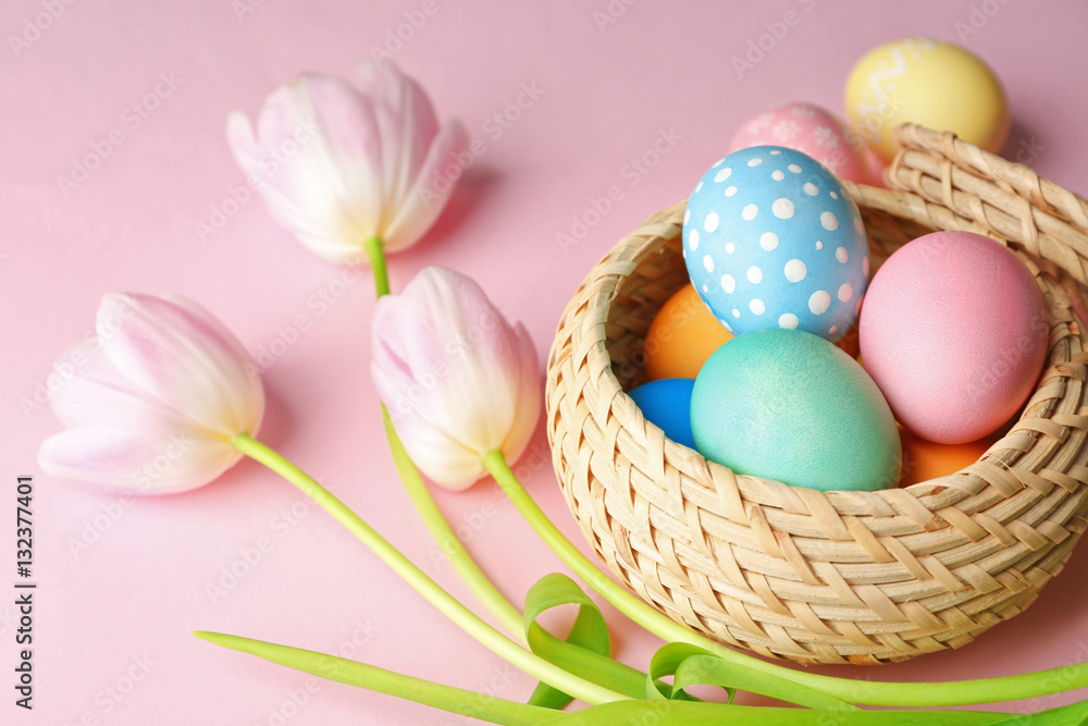 Basket with painted Easter eggs and flowers on pink background Basket with painted Easter eggs and flowers on pink background