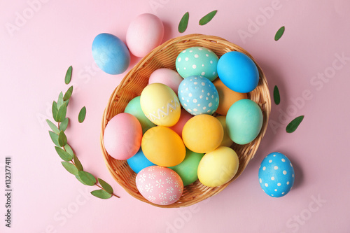 Basket with painted Easter eggs and green leaves on pink background