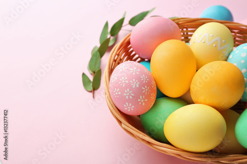 Basket with painted Easter eggs and green leaves on pink background