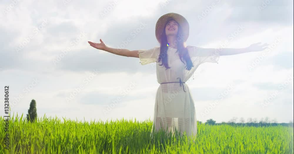 beautiful young woman admires the happy and carefree nature in a meadow at sunset in slow motion