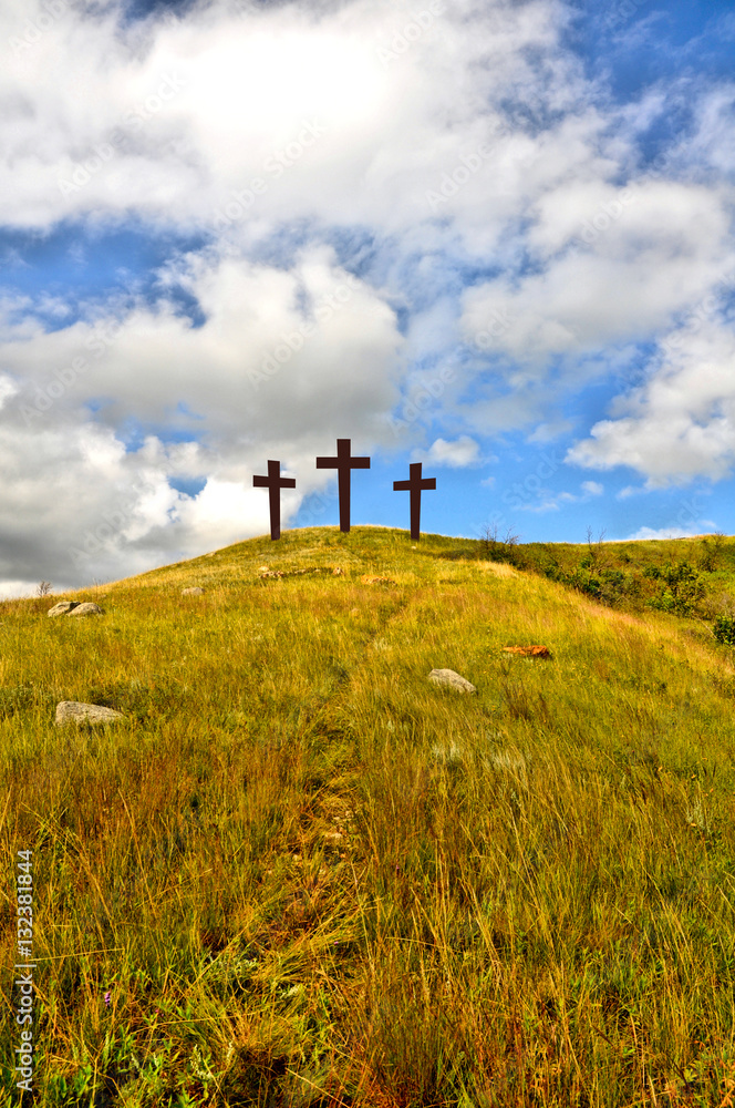 Obraz premium Three crosses on a grassy hill with a bright cloudy blue sky, to represent the crucifixion of Jesus. 