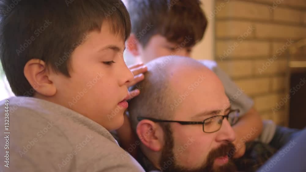 Two boys sit with their dad and watch him use his tablet Two boys sit with their dad and watch him use his tablet