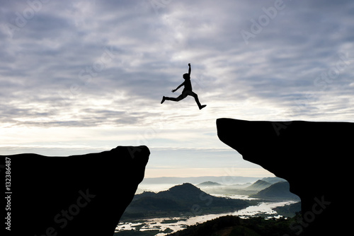 Man jump through the gap between hill.man jumping over cliff on sunset background,Business concept idea photo