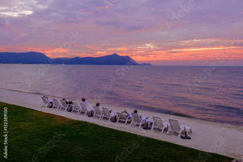 People laying on beach chairs against a beautiful sunset in the