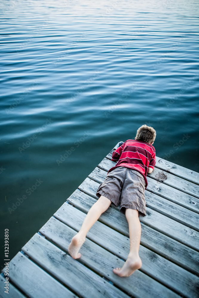 Boy laying on a dock looking at the water Boy laying on a dock looking at the water