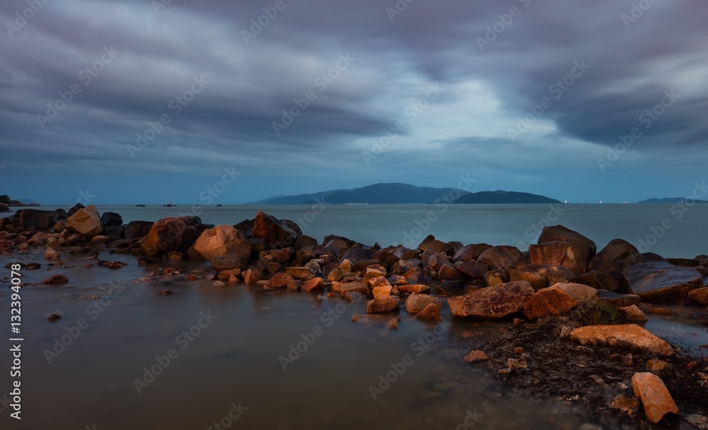 A cloudy evening sky over the south china sea with a rock formation and vinpearl island in the distance, Vietnam.