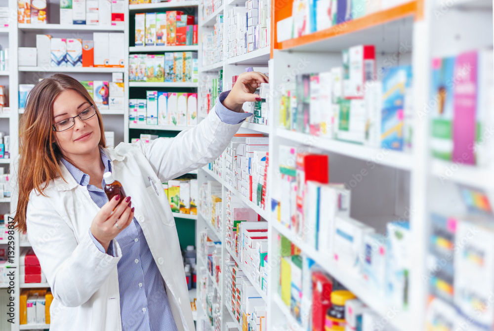 Woman pharmacist holding prescription checking medicine in pharmacy (or drugstore - obrazy, fototapety, plakaty 