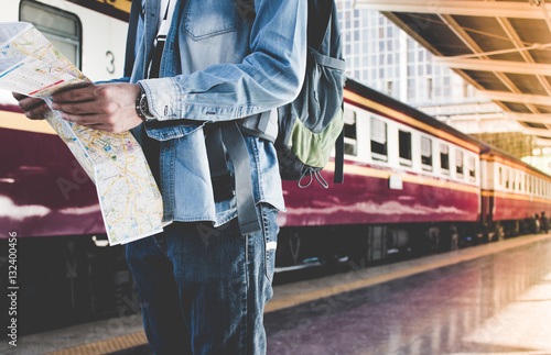 Backpacker waiting for long journey travel at train station with backpack and map on hand. Travel concept with vintage filter effected.