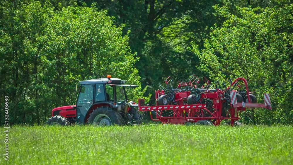 A tractor is leaving the fields with the rotary hay rakes folded up. A