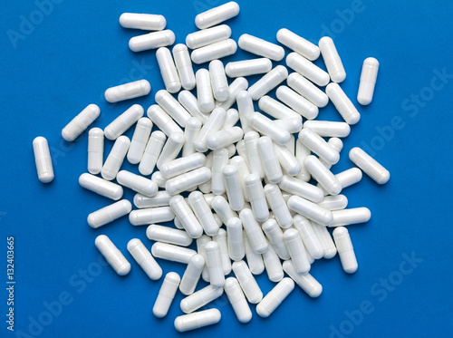 Heap of white capsules on blue background. Top view, high resolution product. Health care concept