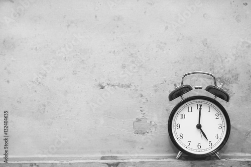 alarm clock showing five o'clock on wooden background, black and white image