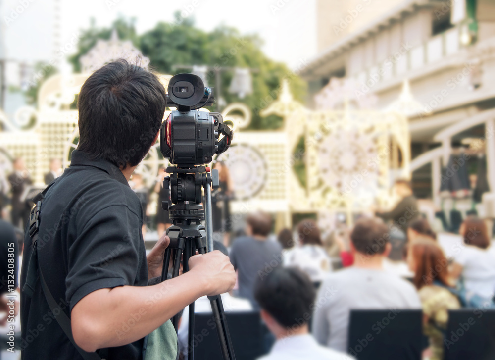 Back of young cameraman using a professional camcorder outdoor  filming music show or mini concert with blur background, Bangkok, Thailand