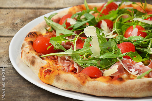 Pizza with prosciutto and rocket salad on wooden table